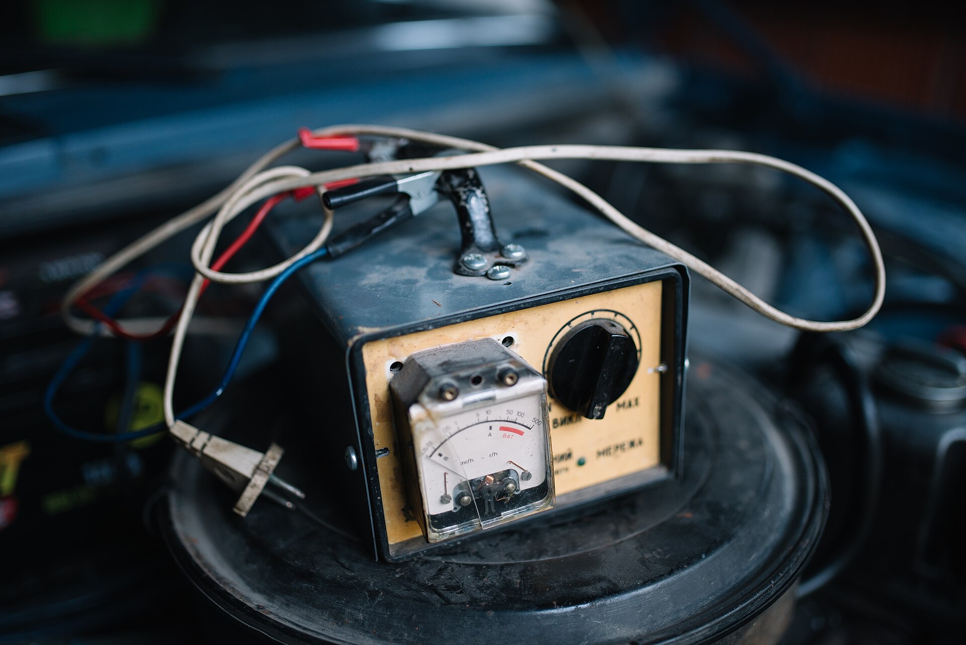 An old battery charger with an analogue ammeter and clamp leads in a garage