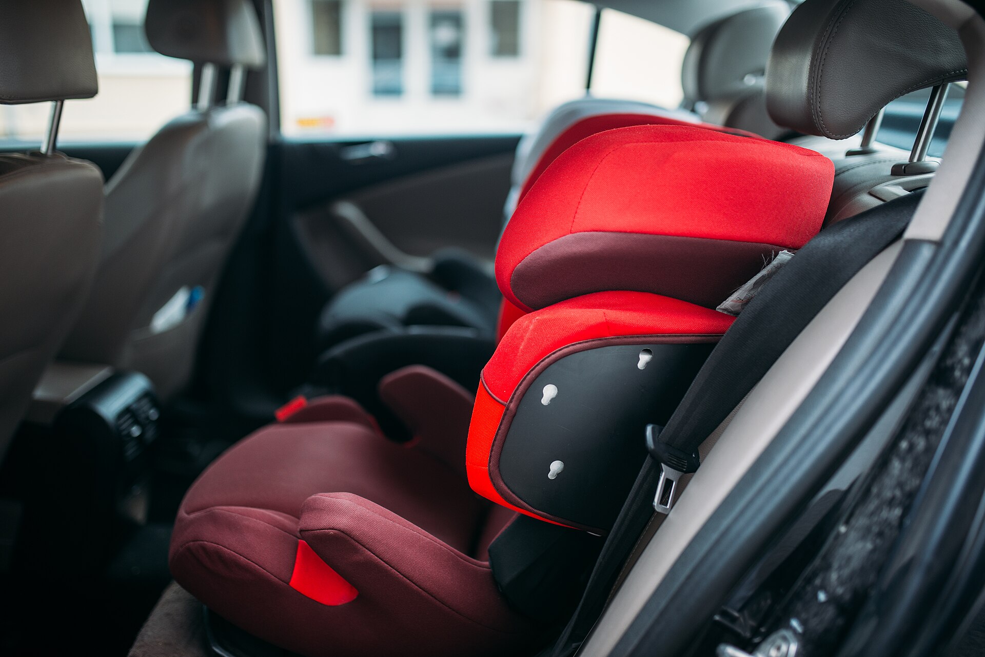 A red child car seat installed on the rear seat of a car