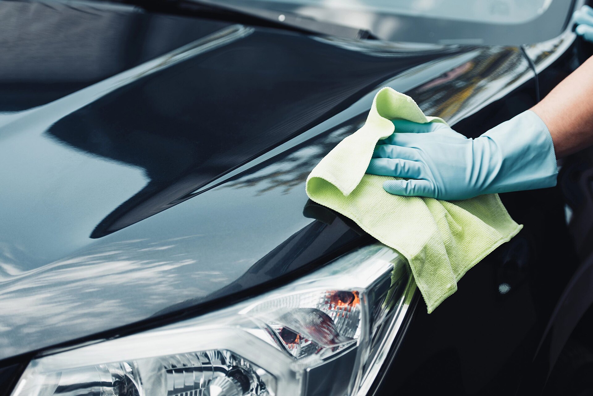 A gloved hand buffing a glossy black car bonnet with a microfibre cloth