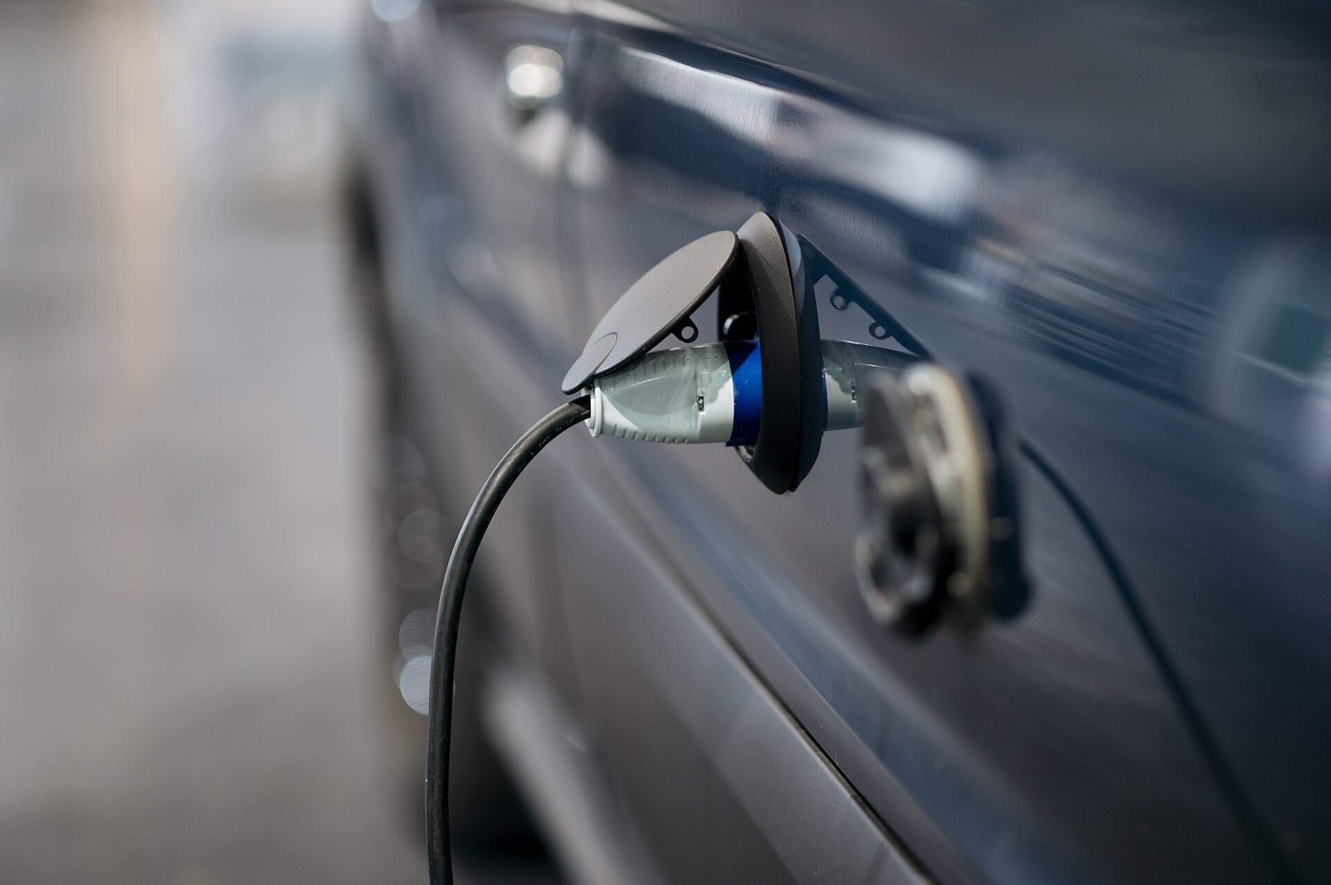 A charging cable plugged into the charge port of a dark blue electric car