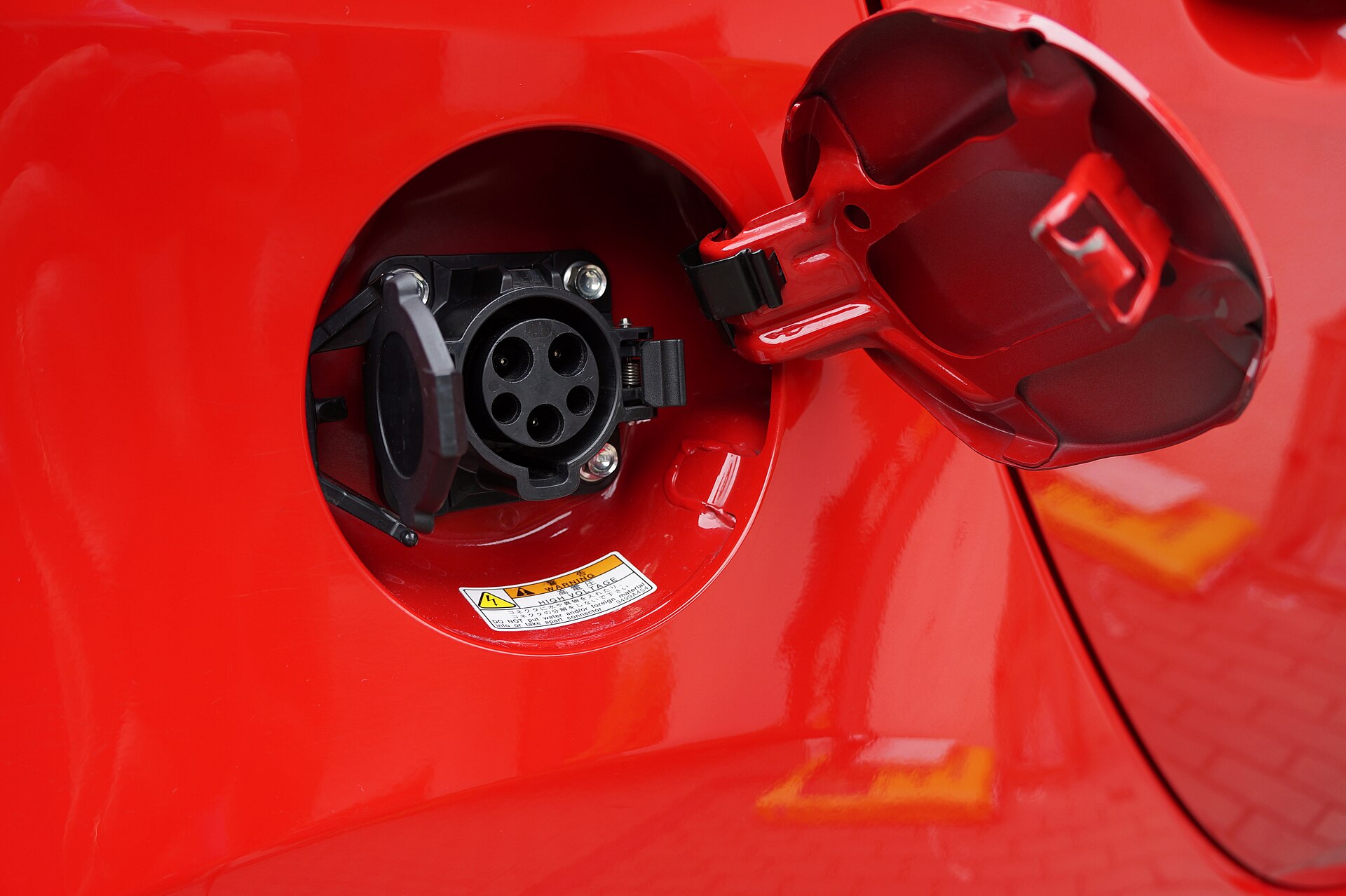 An open charge-port door revealing a J1772 socket on a red electric car