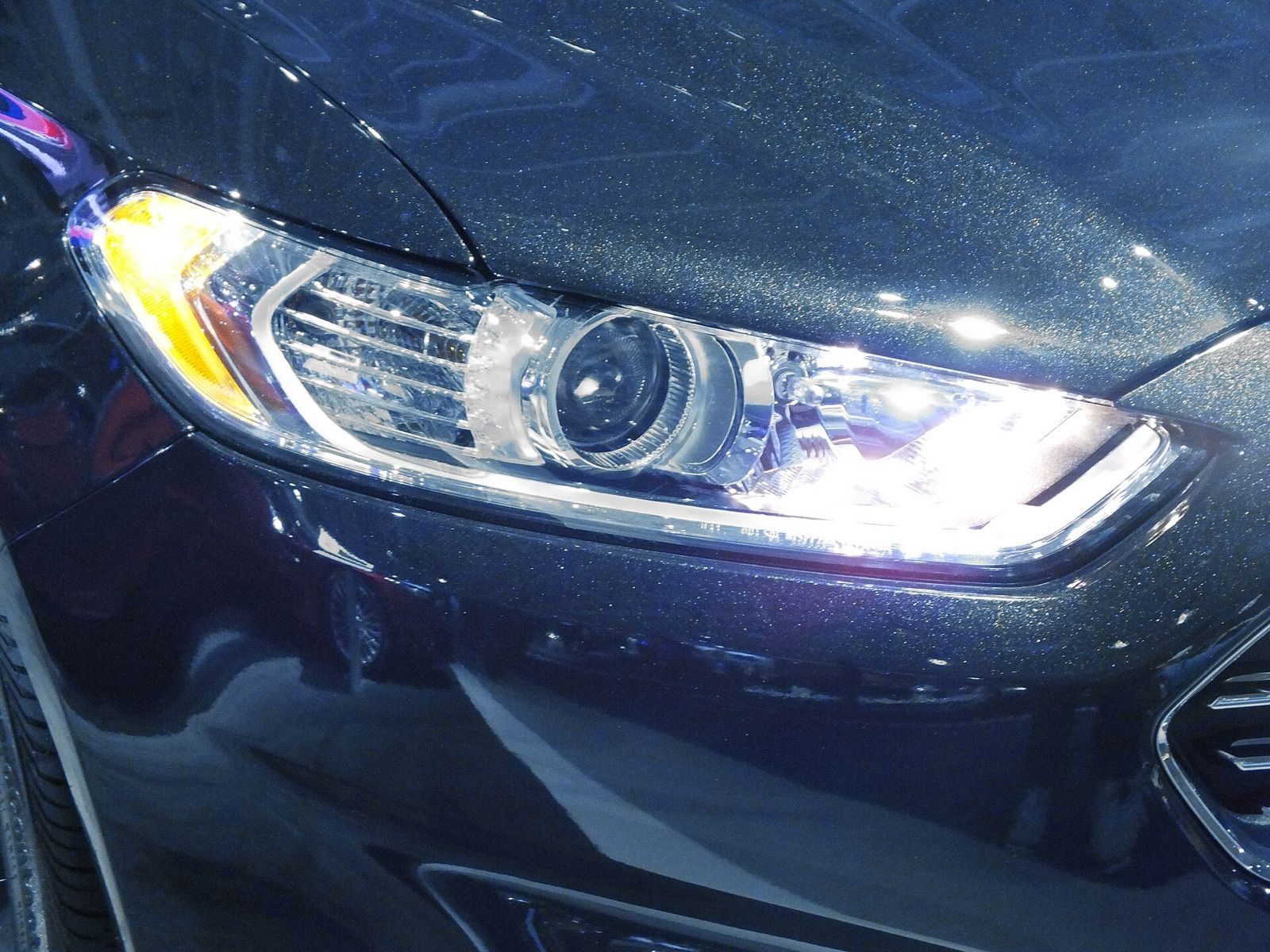 A projector headlight with its lens and daytime running light strip on a dark car