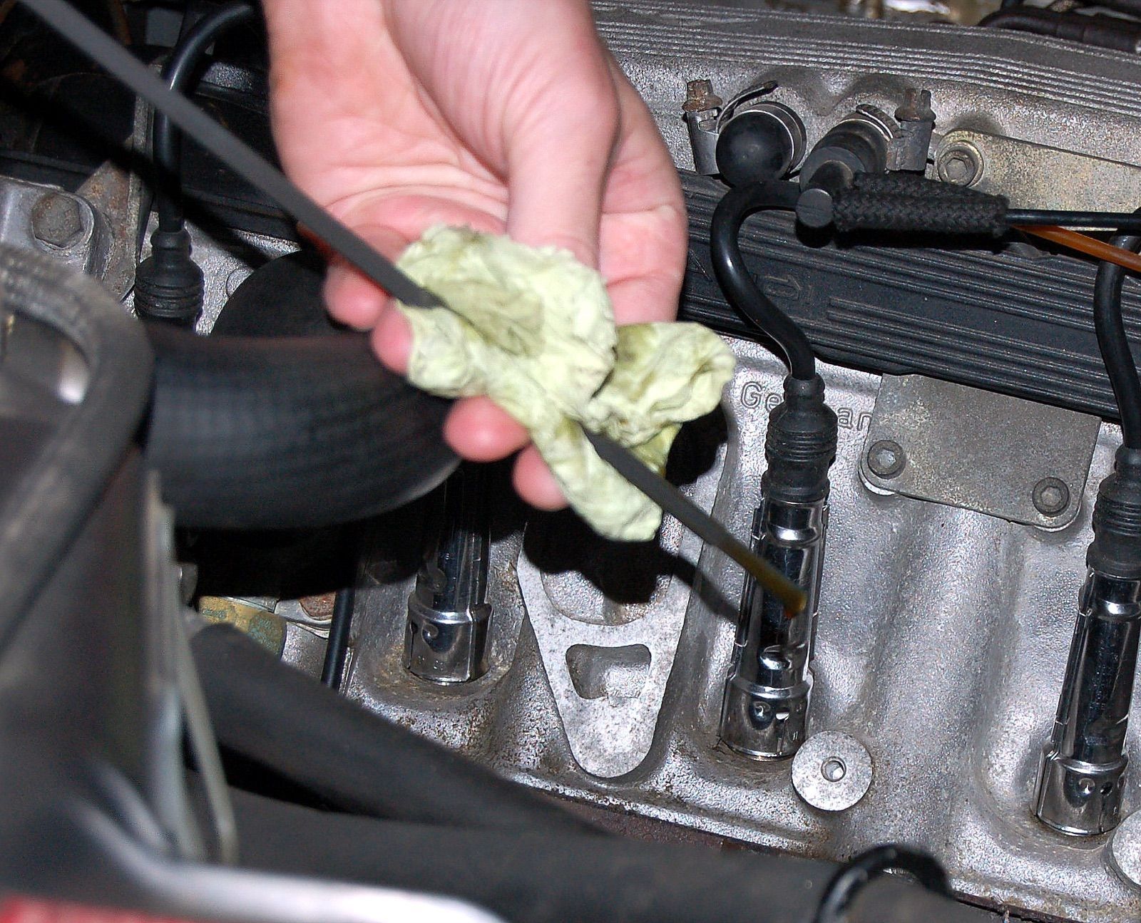 A hand wiping an engine oil dipstick with a rag to check the level