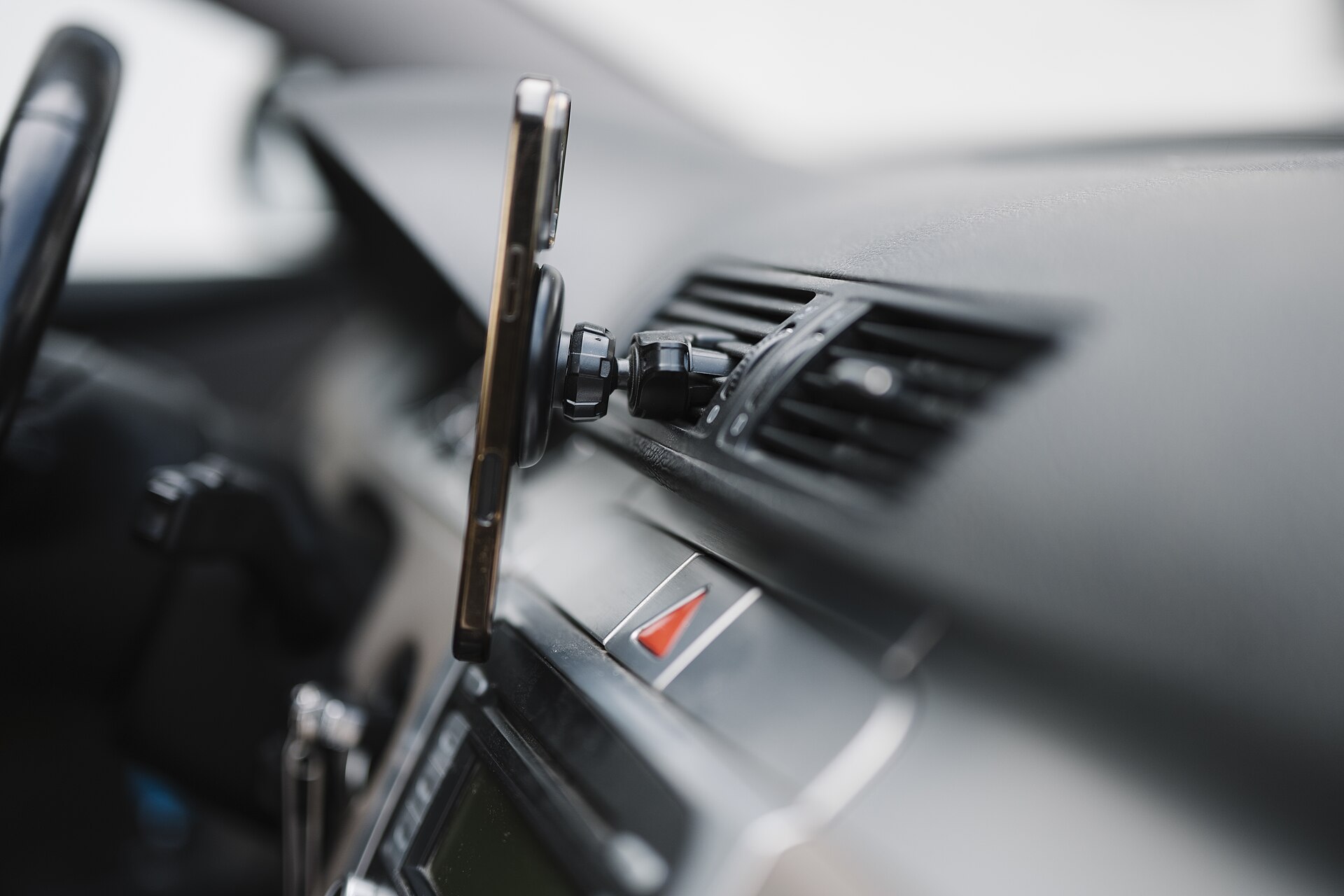 A smartphone held on a mount beside a car's dashboard air vents