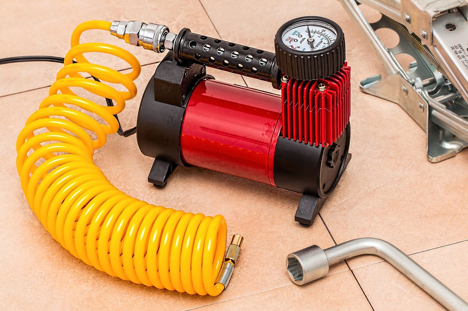 A 12-volt tyre compressor with a pressure gauge and coiled yellow air hose beside a wheel wrench