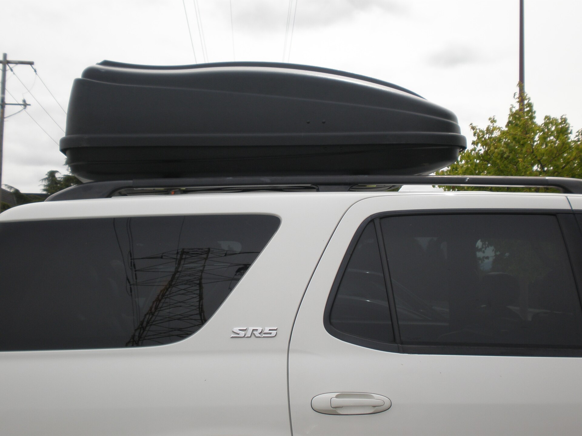 A black cargo box mounted on crossbars on the roof of a white SUV