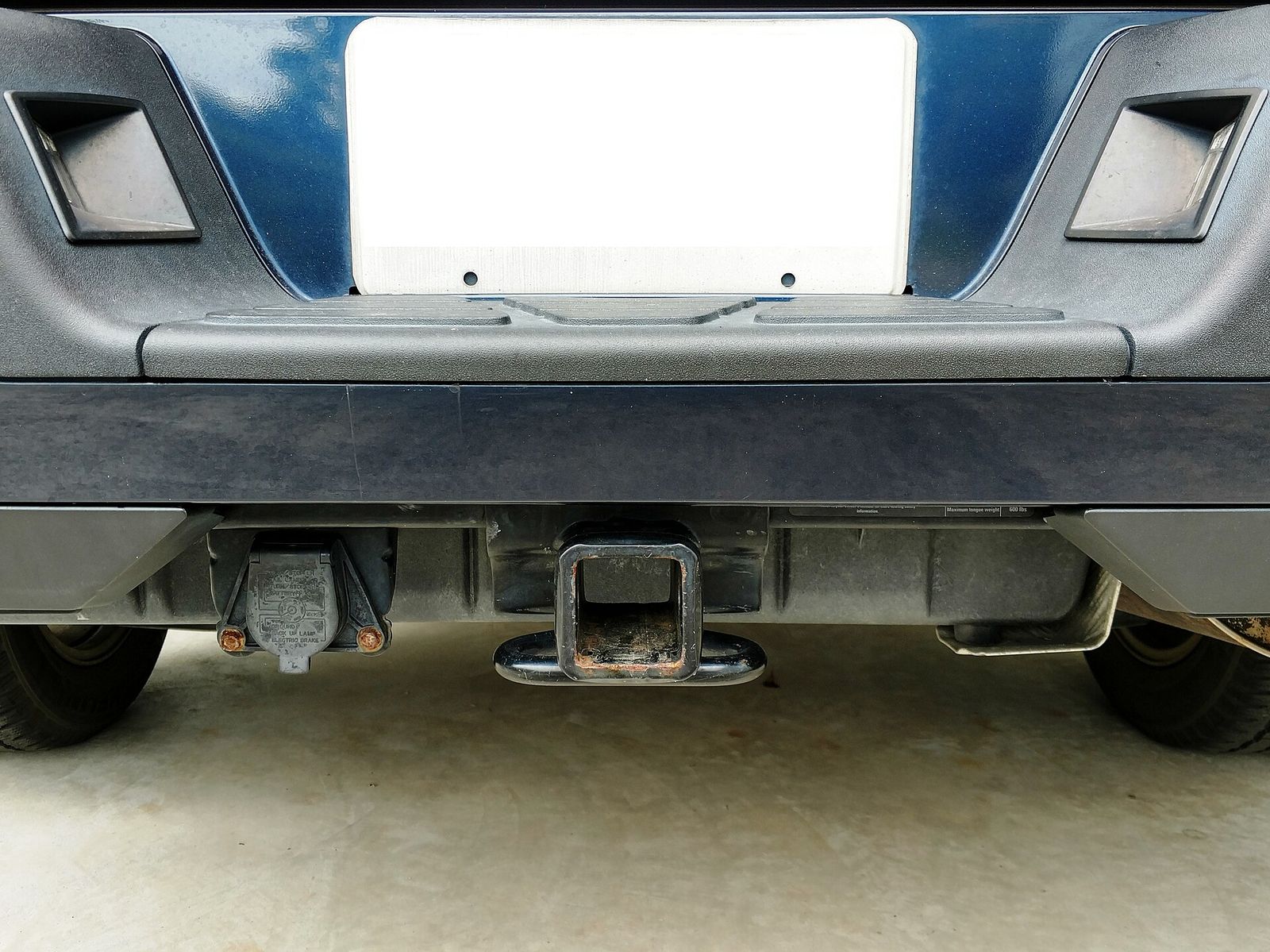 A square receiver-style tow hitch under a pickup's rear bumper next to a 7-pin trailer connector