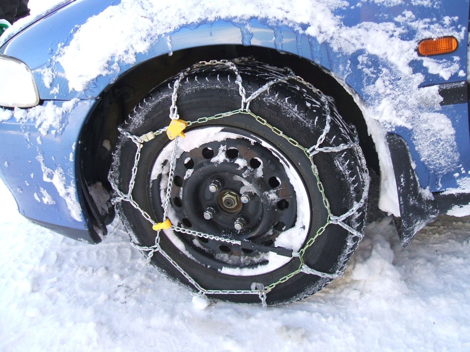 Snow chain fitted over a car's front tyre on a snowy road
