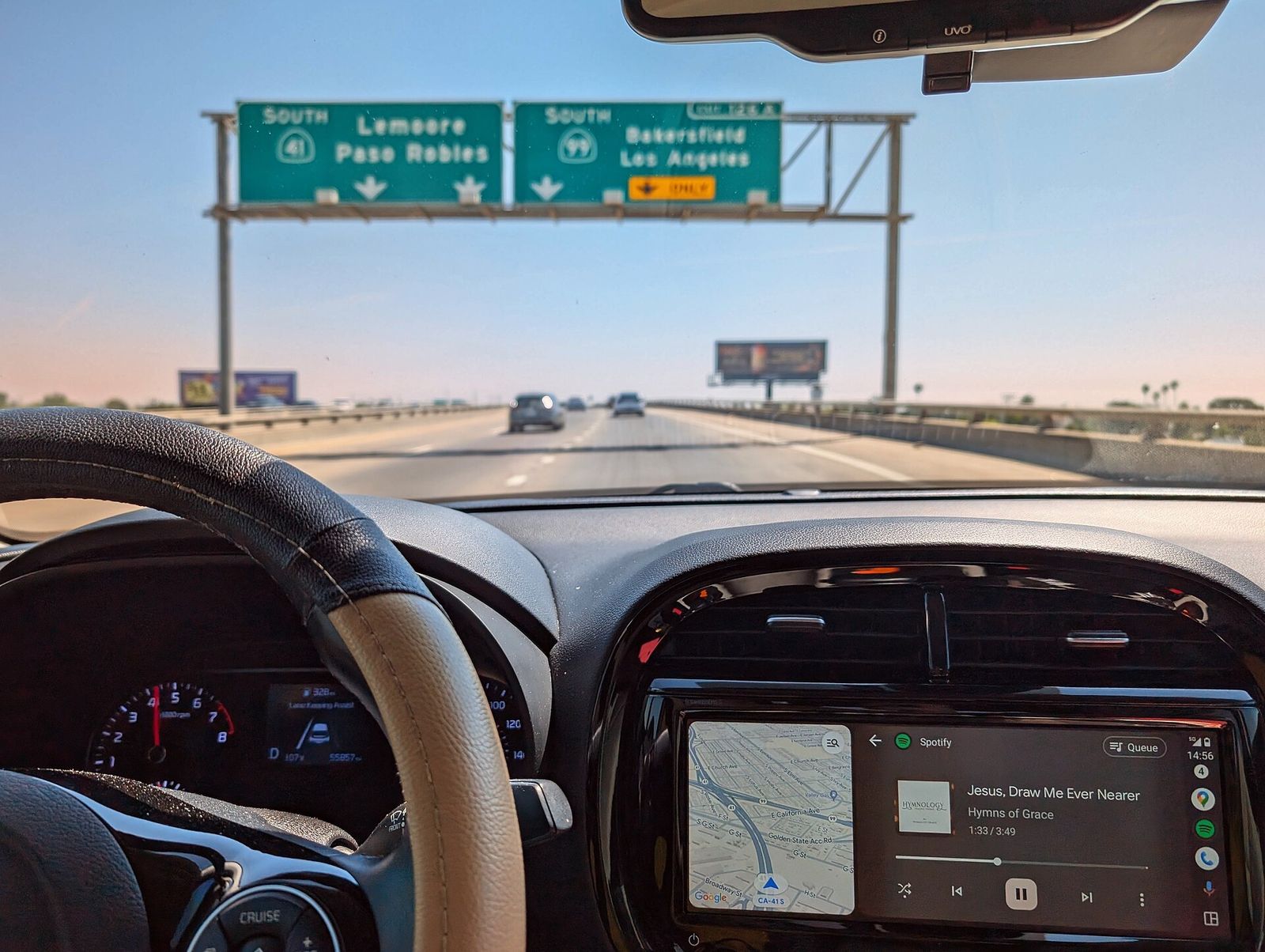 A car's dashboard touchscreen showing a phone-projected map and music during a highway drive