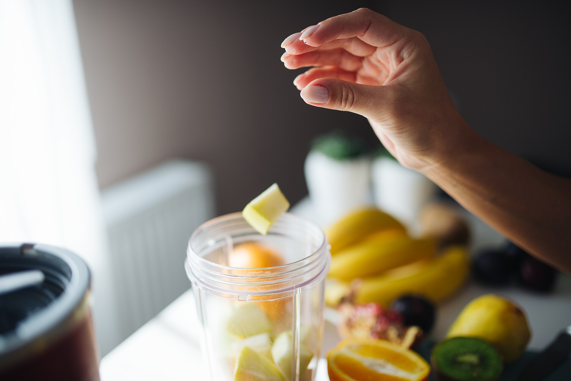 Fruit being added to a personal blender cup on a kitchen counter