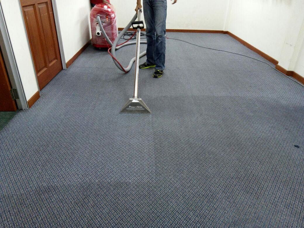 A carpet extraction wand leaving a cleaner stripe across a blue-grey carpet