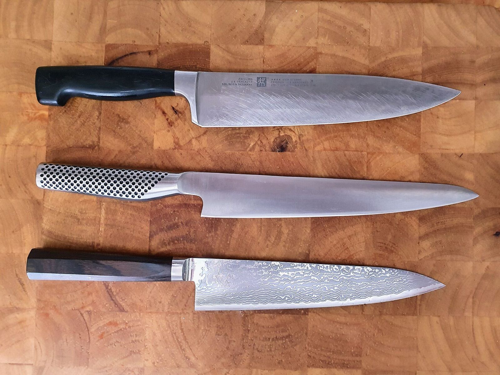 Three chef's knives with different handles on an end-grain cutting board