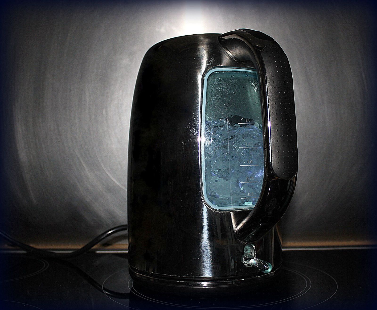 Black electric kettle with a clear water window, lit against a brushed-metal background