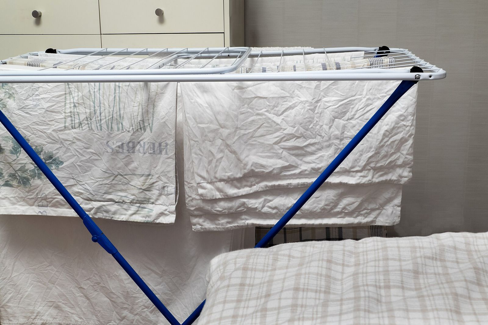 White sheets and pillowcases drying on a folding winged clothes rack indoors