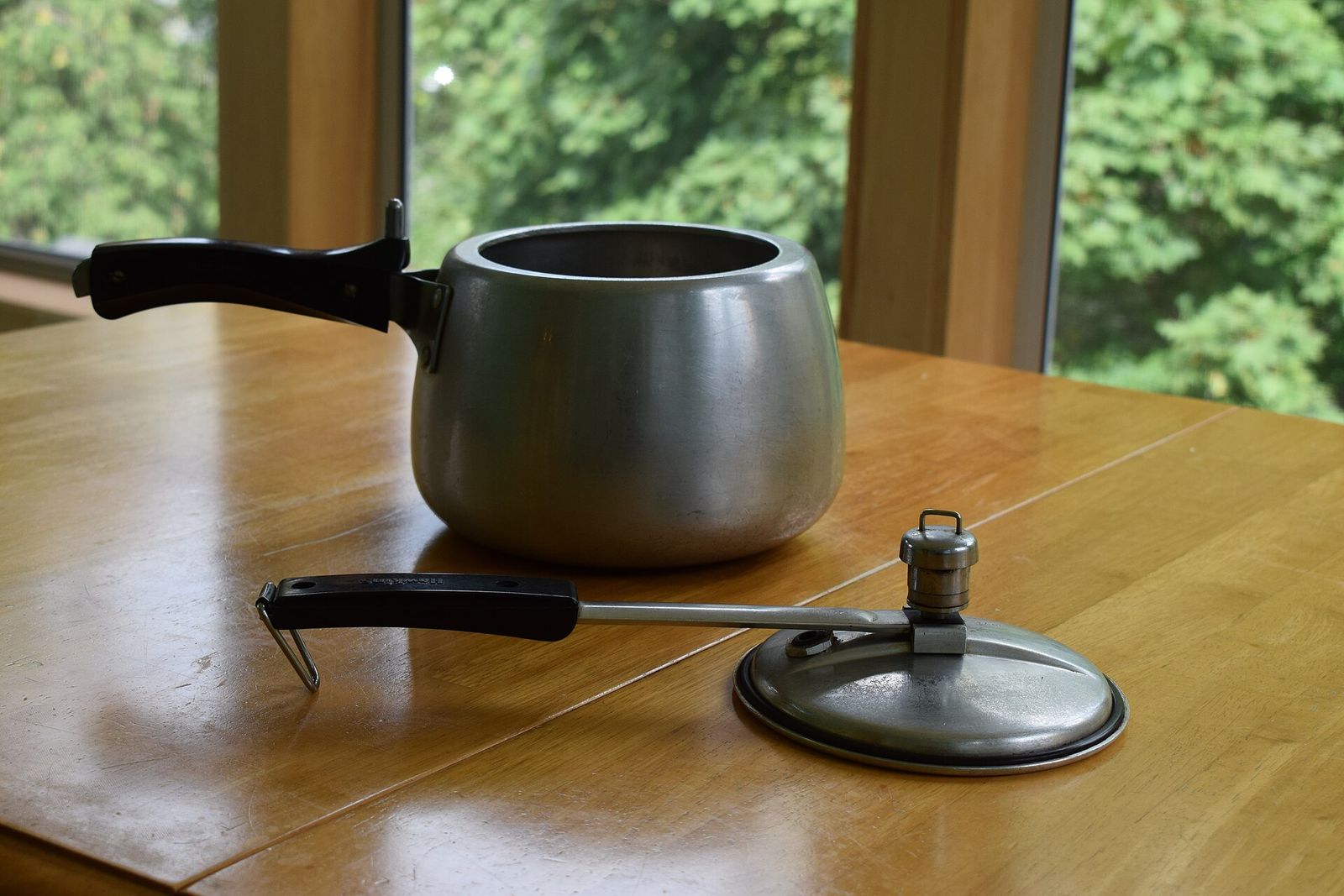 Stovetop pressure cooker with its lid and weighted valve set beside it on a wooden table