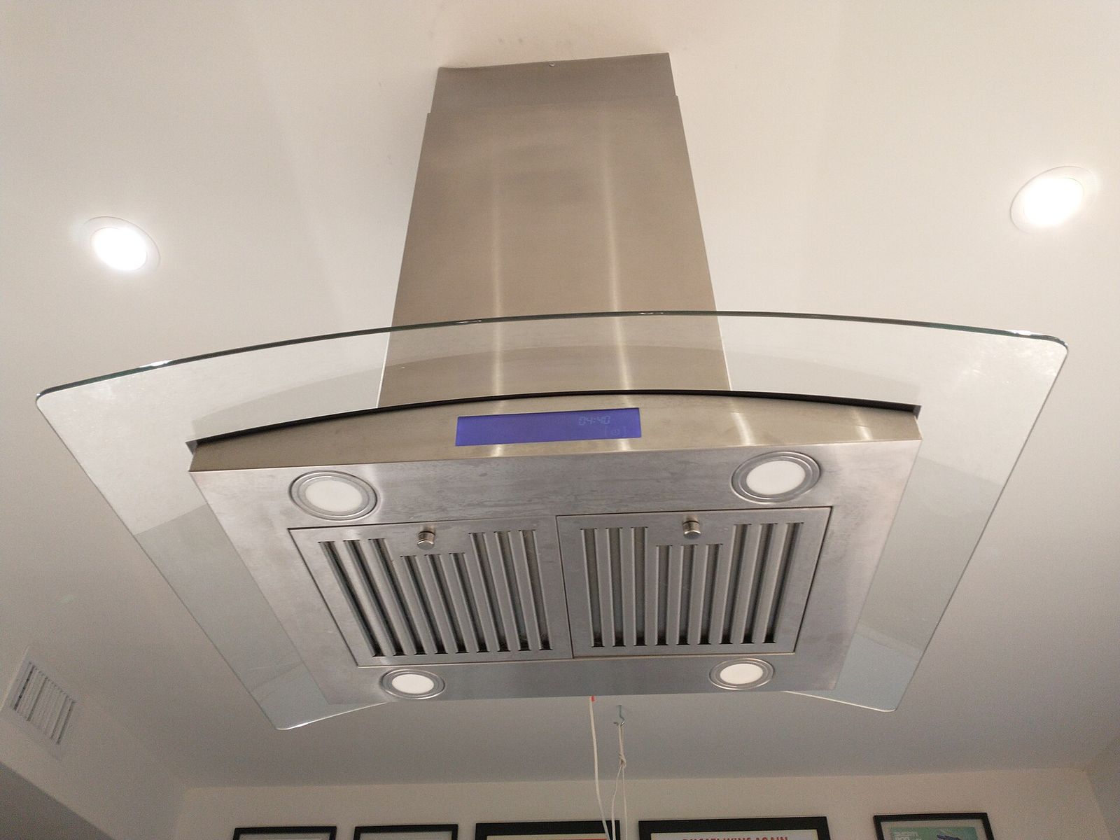Stainless steel island range hood with a glass canopy, baffle filters and lights, seen from below