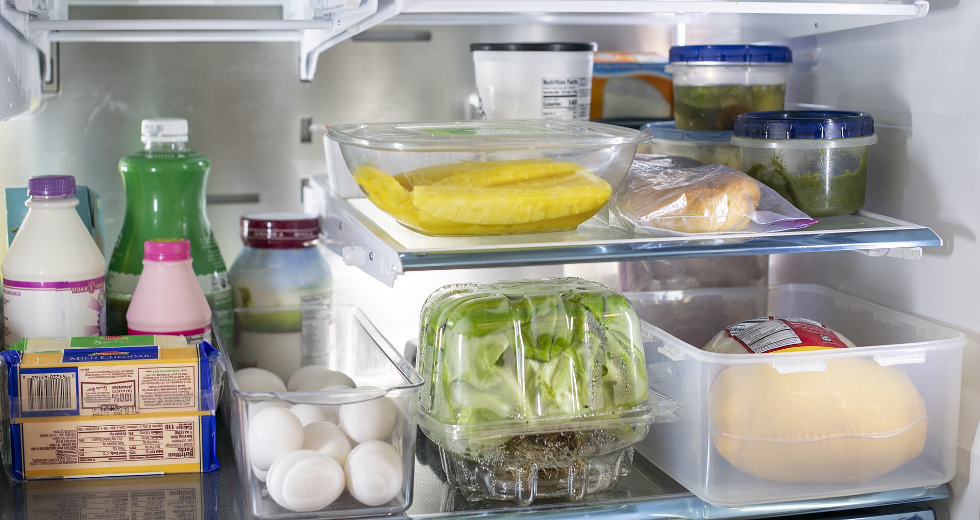 Glass shelves and clear crisper drawers inside a refrigerator, holding eggs, lettuce, cheese and covered leftovers