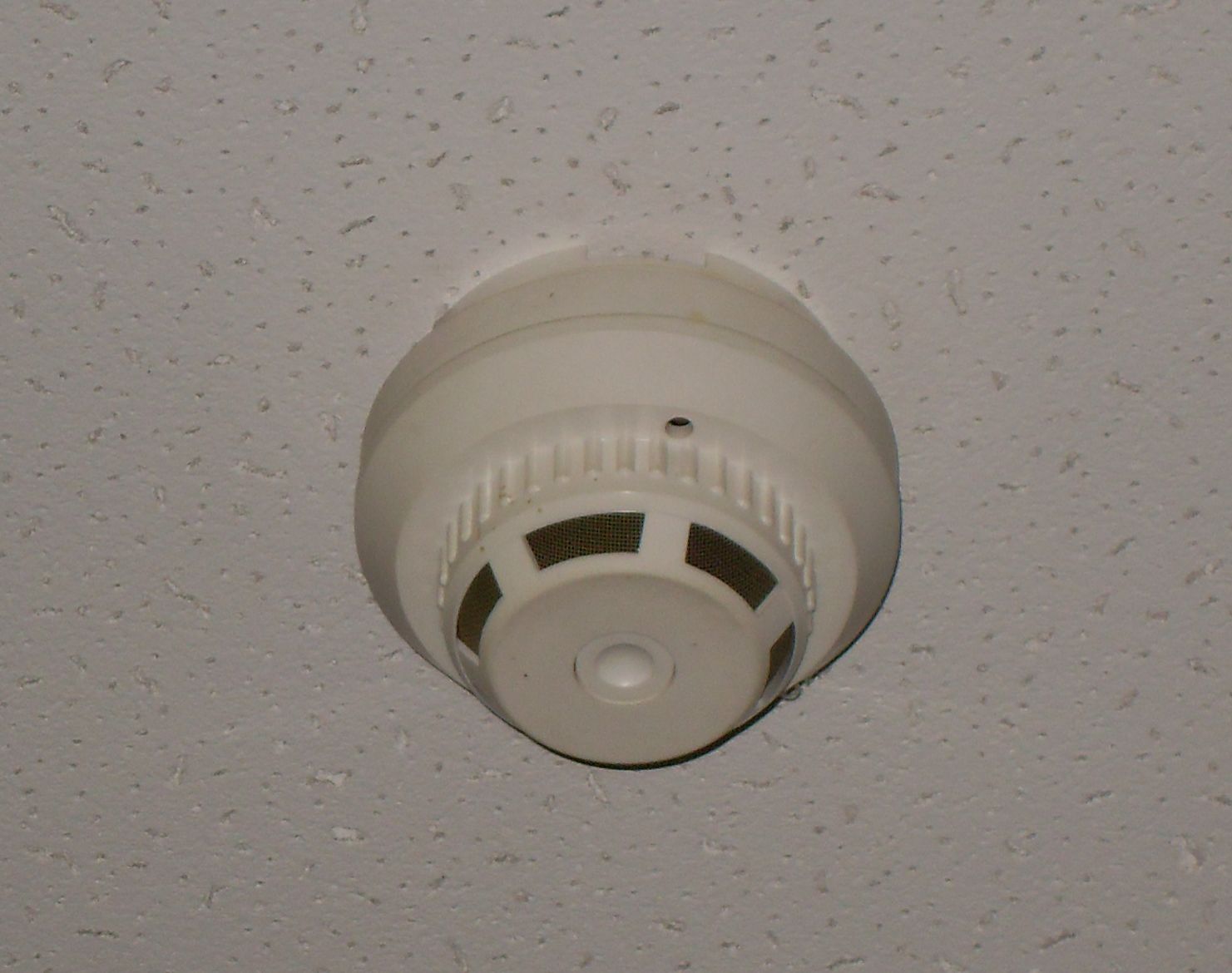 A white smoke detector mounted on a textured ceiling