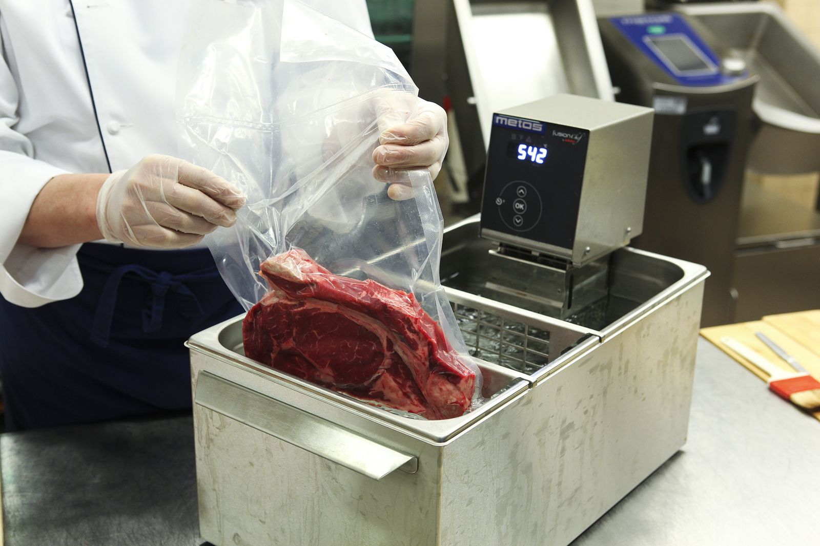 Vacuum-bagged beef being lowered into a water bath heated by an immersion circulator