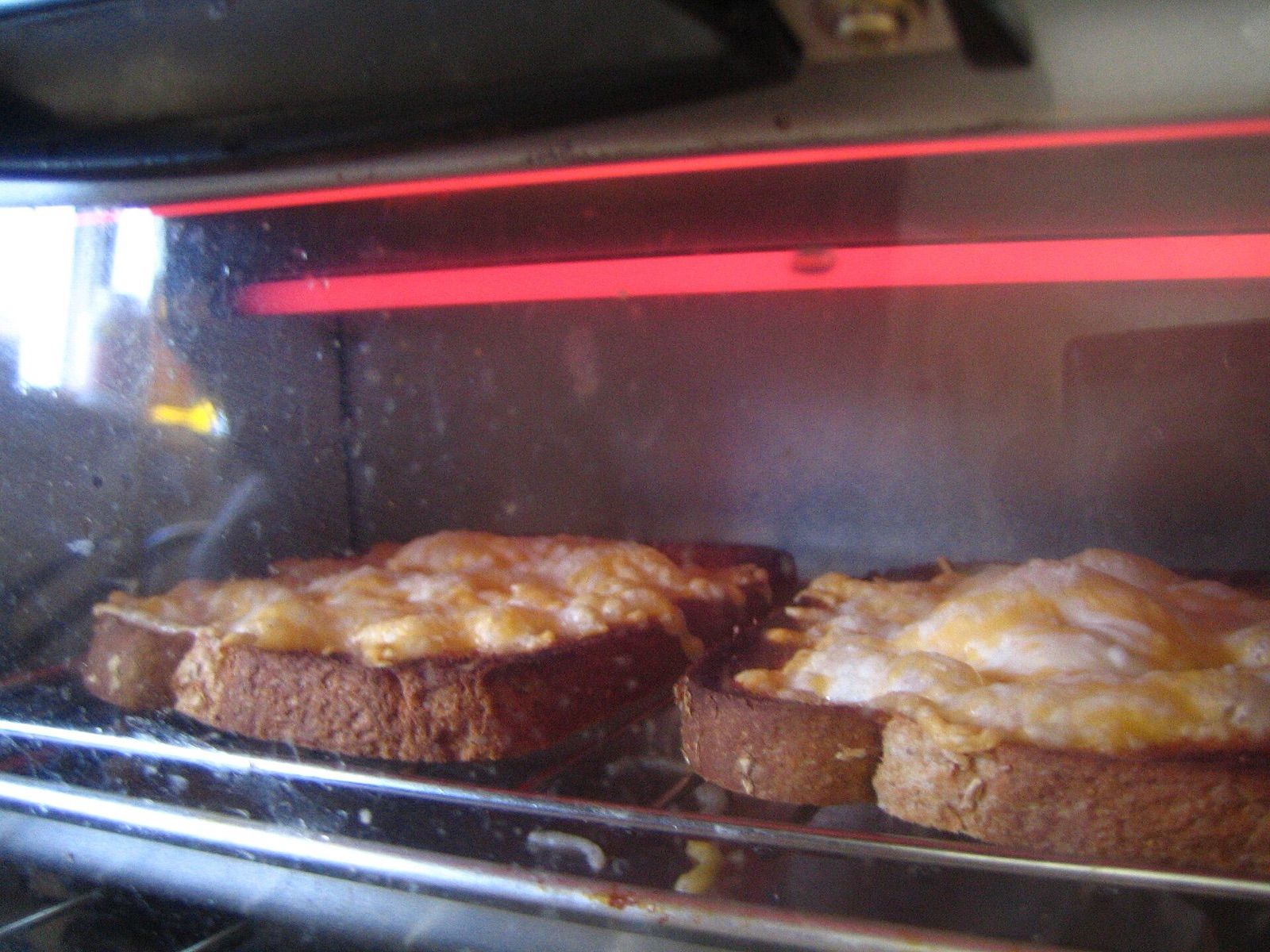 Cheese on toast browning under the glowing top element inside a toaster oven