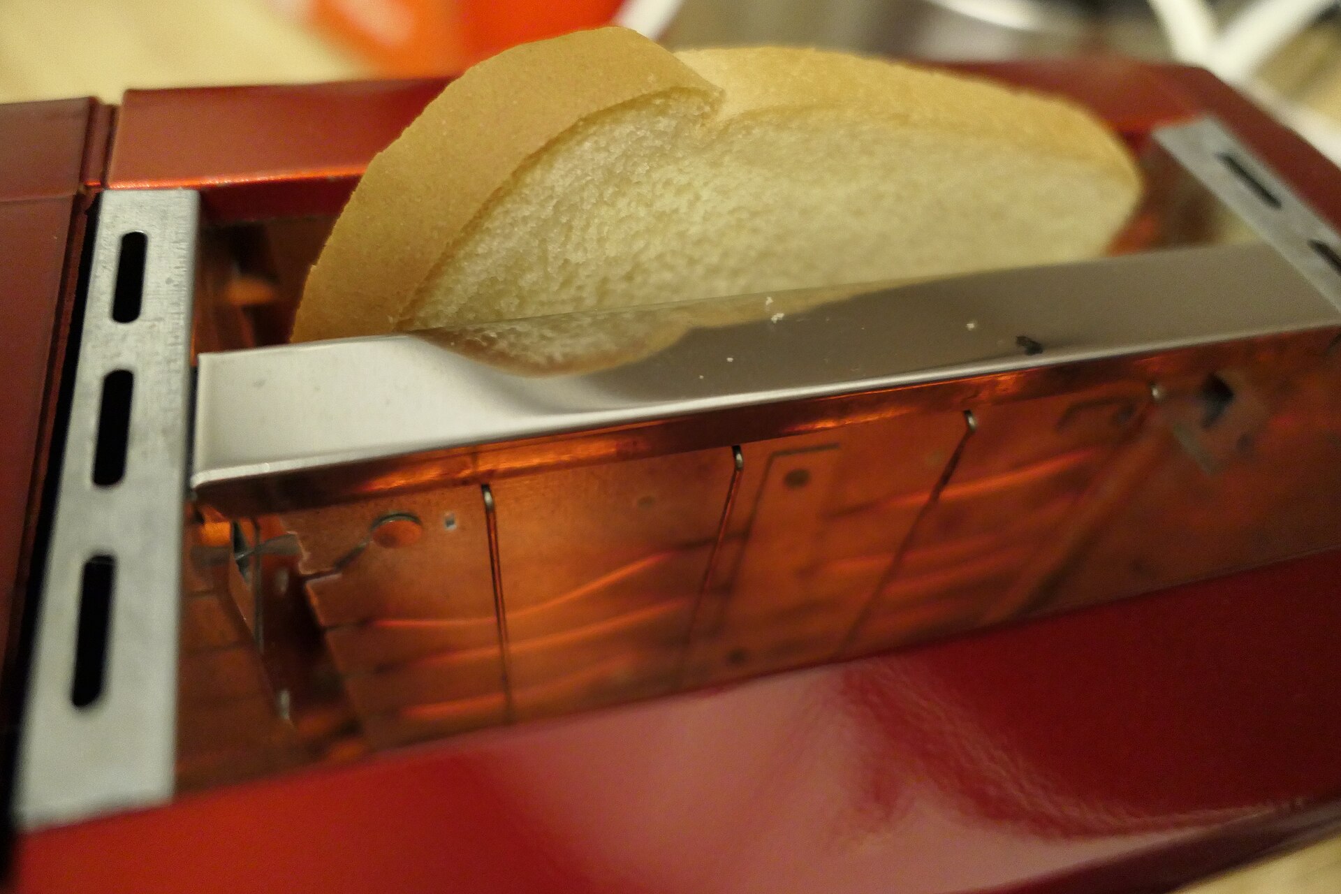 Two slices of bread standing in the slot of a red pop-up toaster