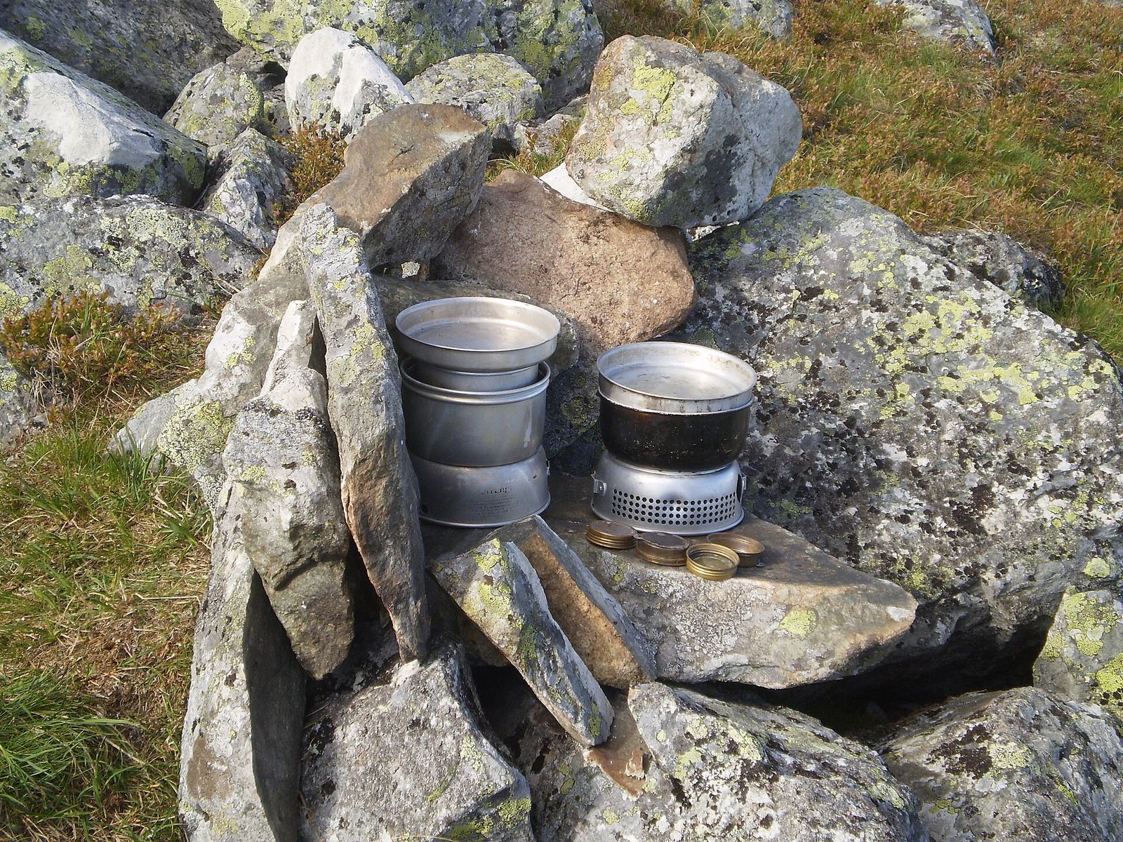 Two compact camping stove sets with nesting pans on lichen-covered rocks in the hills