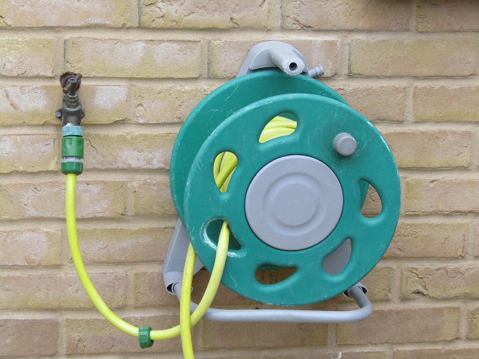 Wall-mounted garden hose reel beside an outdoor tap on a brick wall