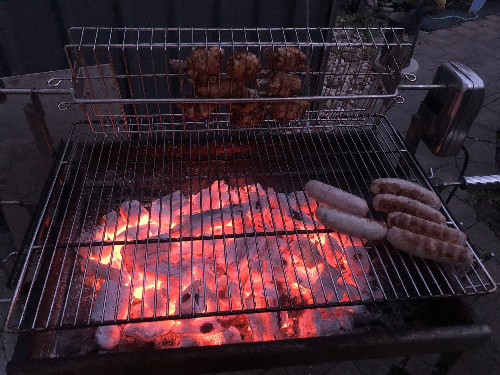 Sausages and chicken cooking over glowing charcoal on a barbecue grill