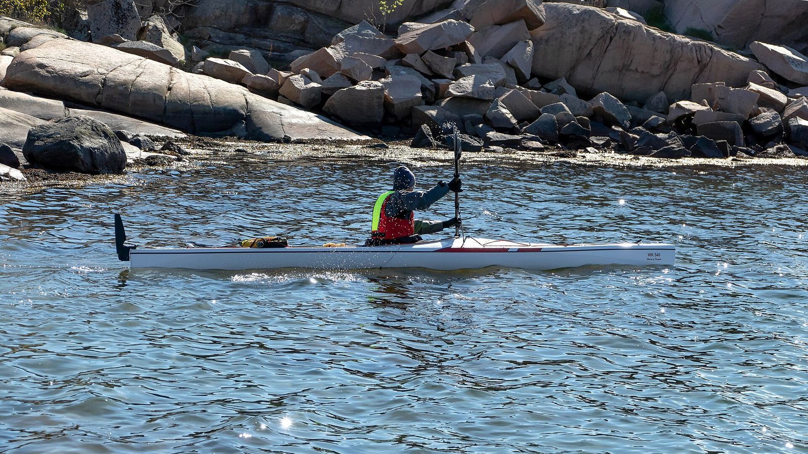 Paddler wearing a buoyancy aid in a white sea kayak near a rocky shoreline