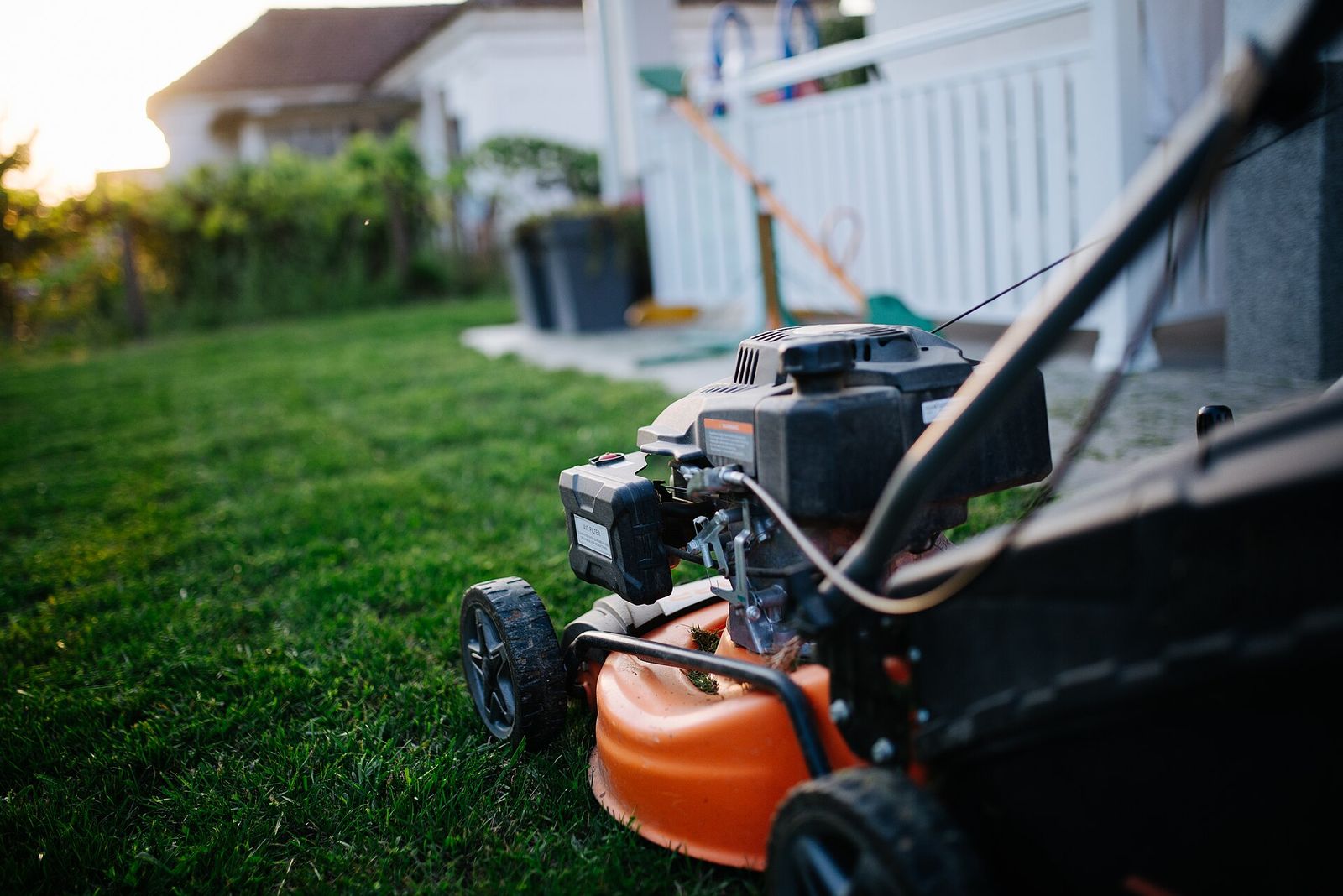 A walk-behind gas lawn mower on a freshly cut lawn beside a house