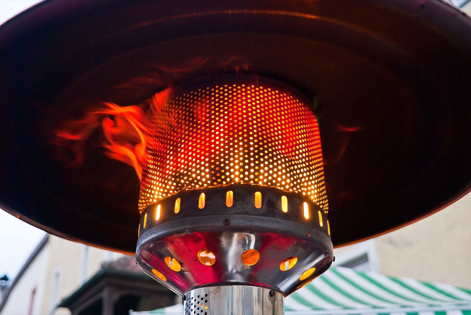 The glowing burner and reflector hood of a gas mushroom-style patio heater
