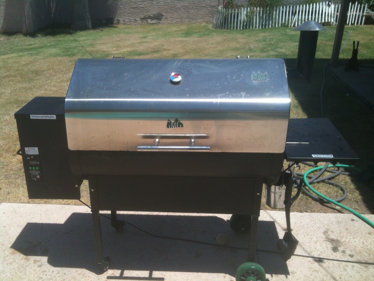 A stainless steel pellet grill with its side hopper and controller on a backyard patio
