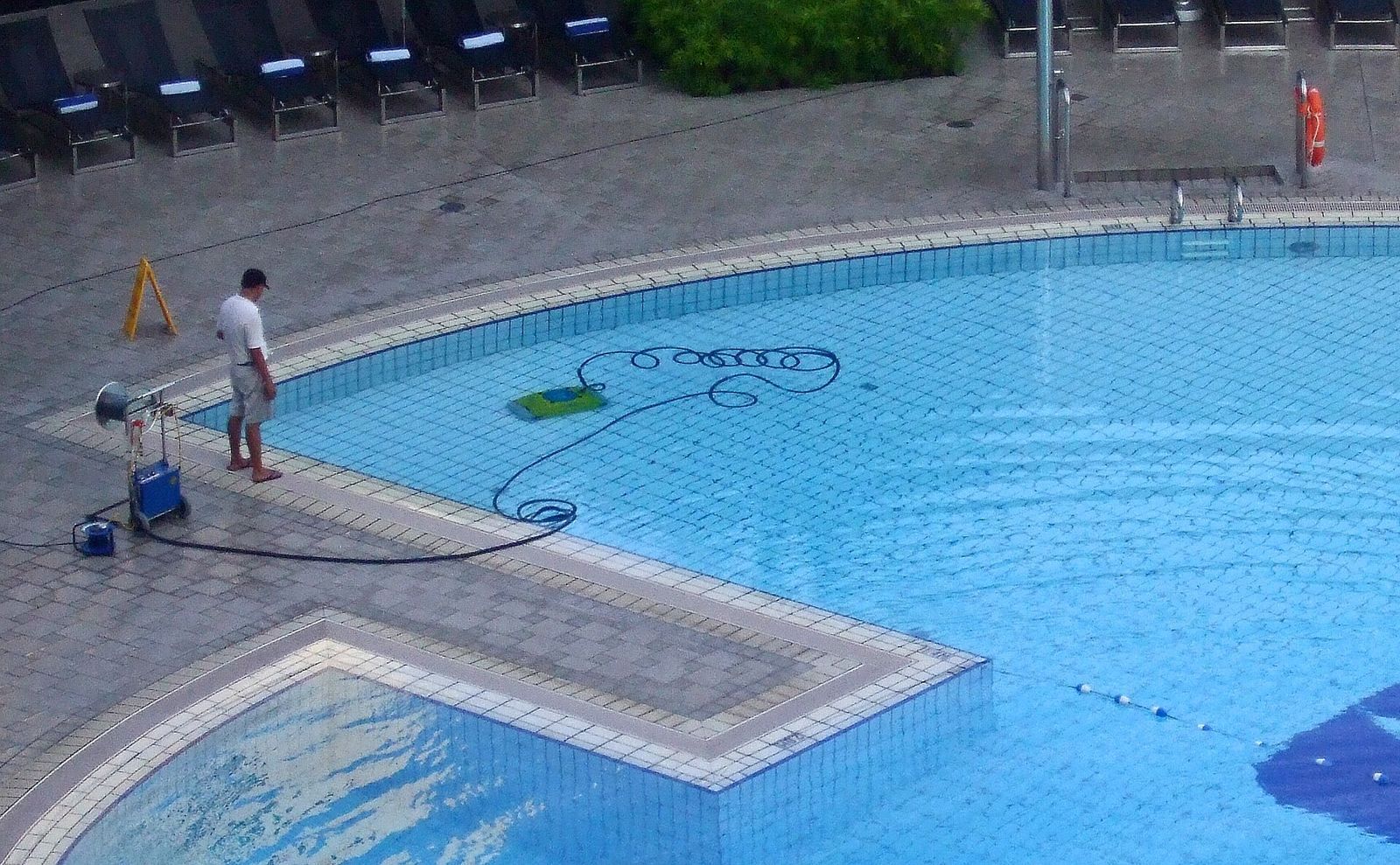 Robotic pool cleaner on its cable working on the floor of an outdoor swimming pool