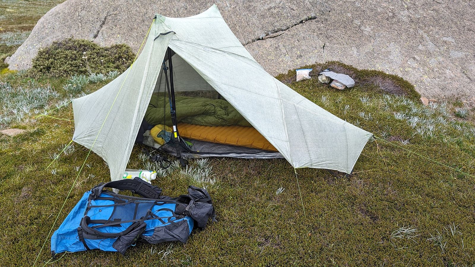 Green sleeping bag on an orange sleeping mat inside a small tent, with a backpack in front