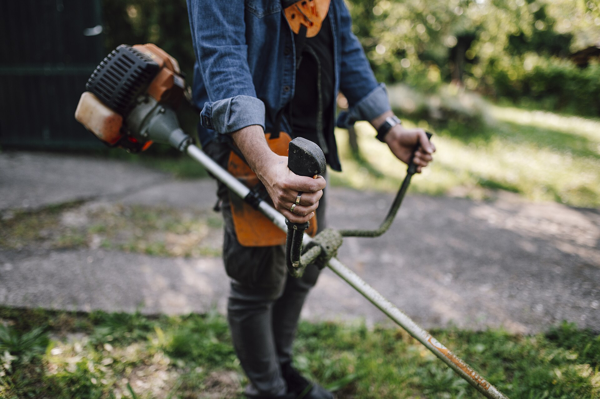 A gardener cutting grass along a path with a gas string trimmer