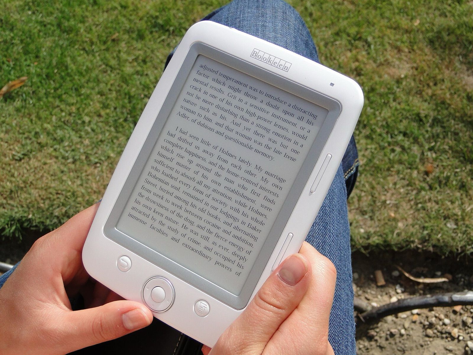 Hands holding a small e-reader showing a page of text outdoors