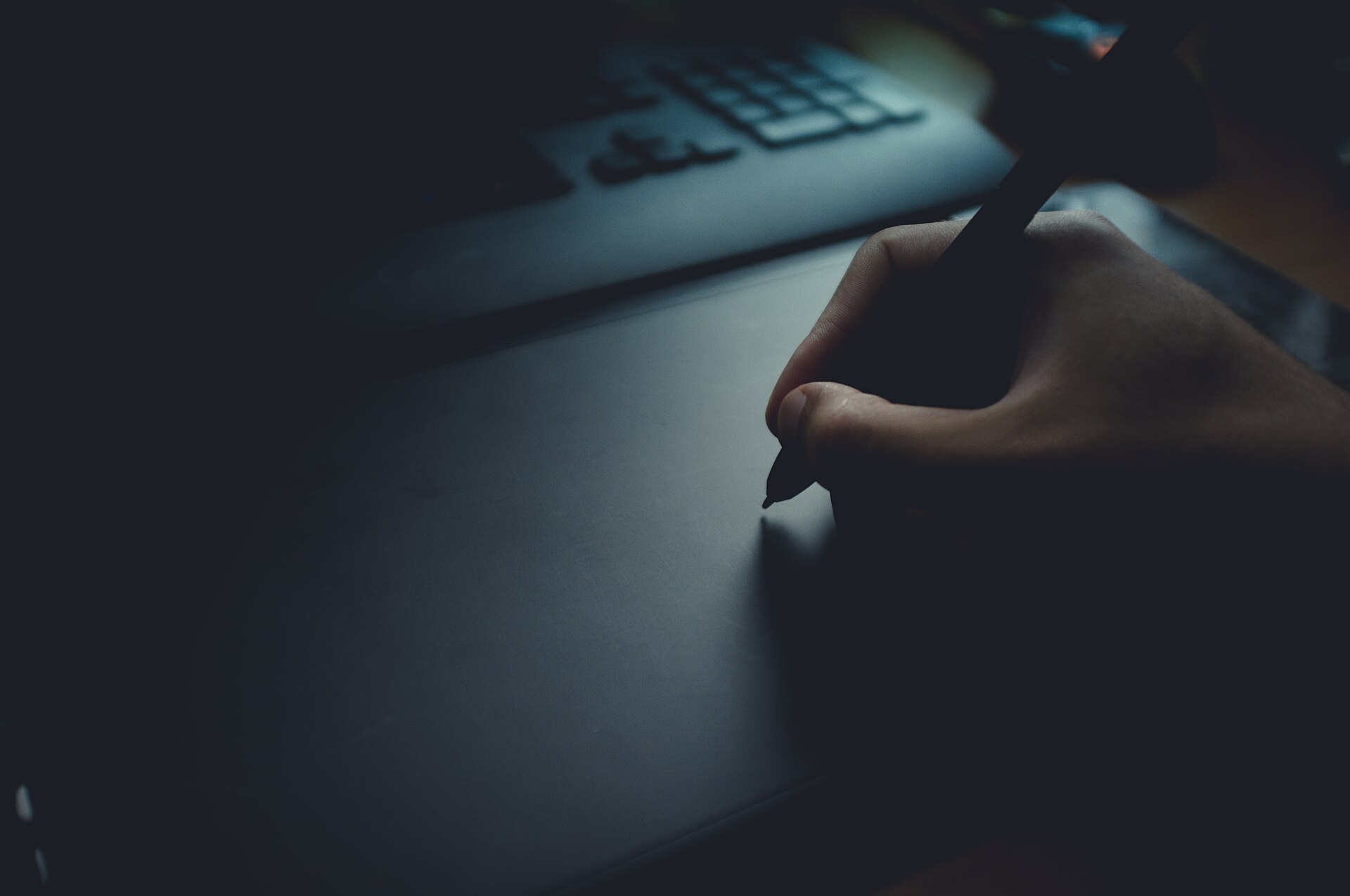 A hand drawing with a stylus on a screenless graphics tablet beside a keyboard