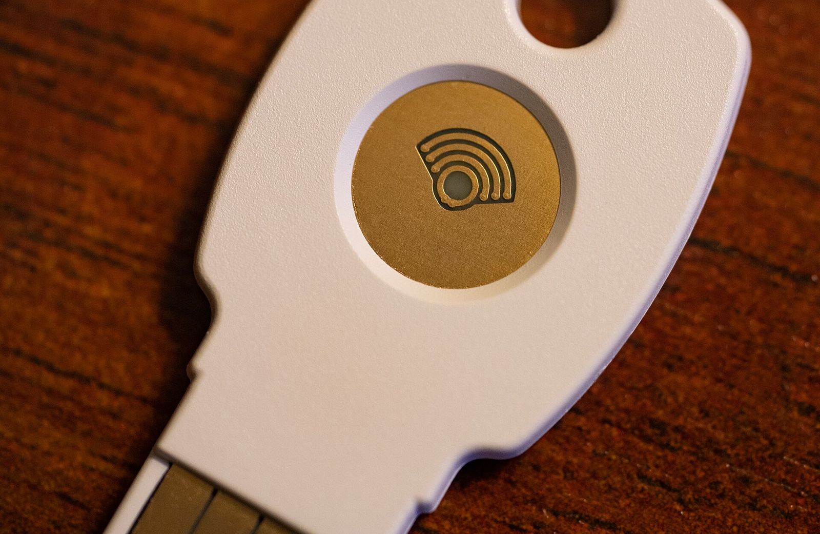 Close-up of a white hardware security key with a gold touch sensor on a wooden table