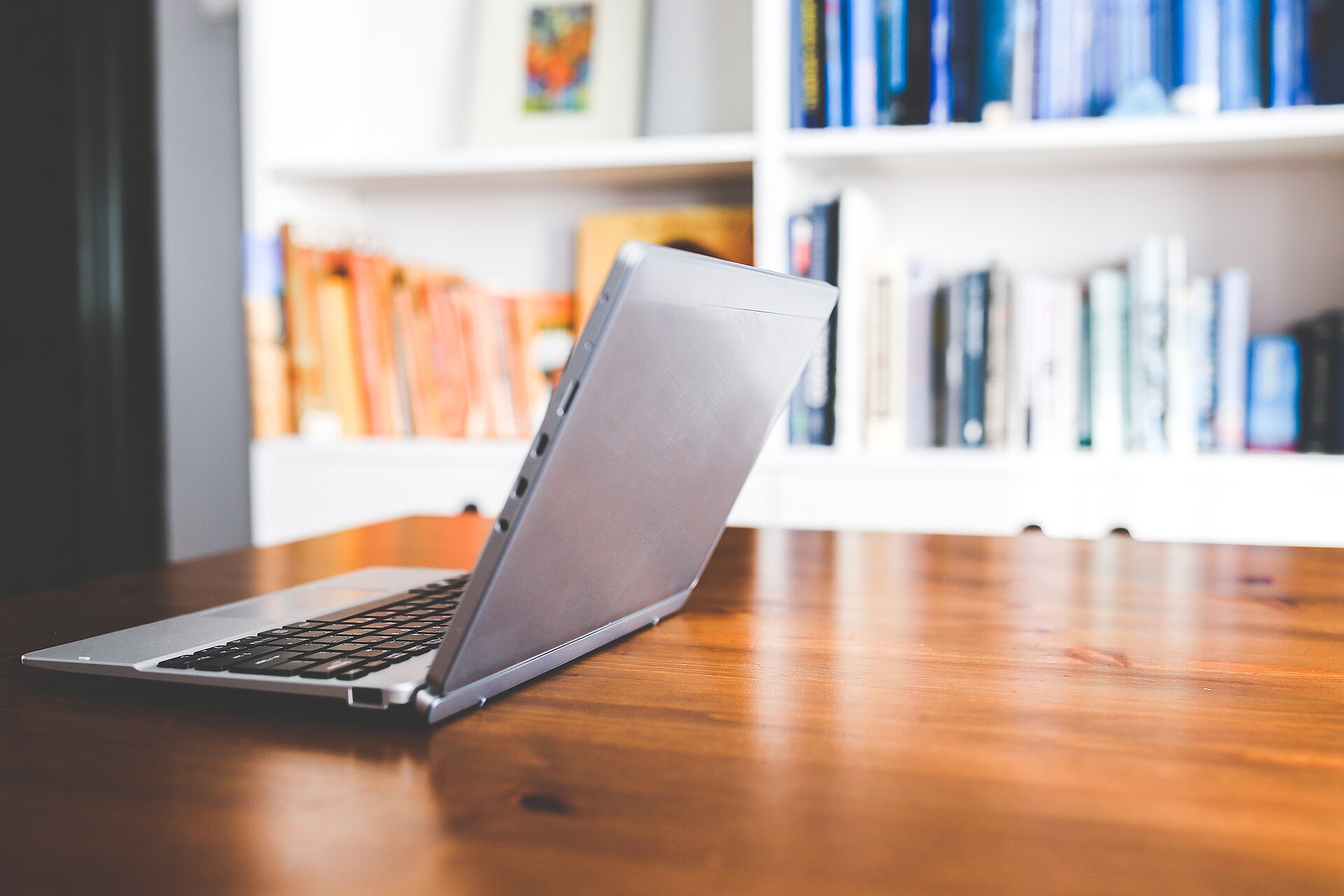 Thin laptop open on a wooden desk in front of bookshelves
