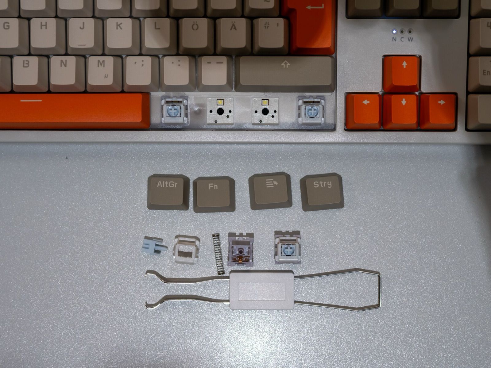 A mechanical keyboard with keycaps removed, showing switches, a spring and a keycap puller
