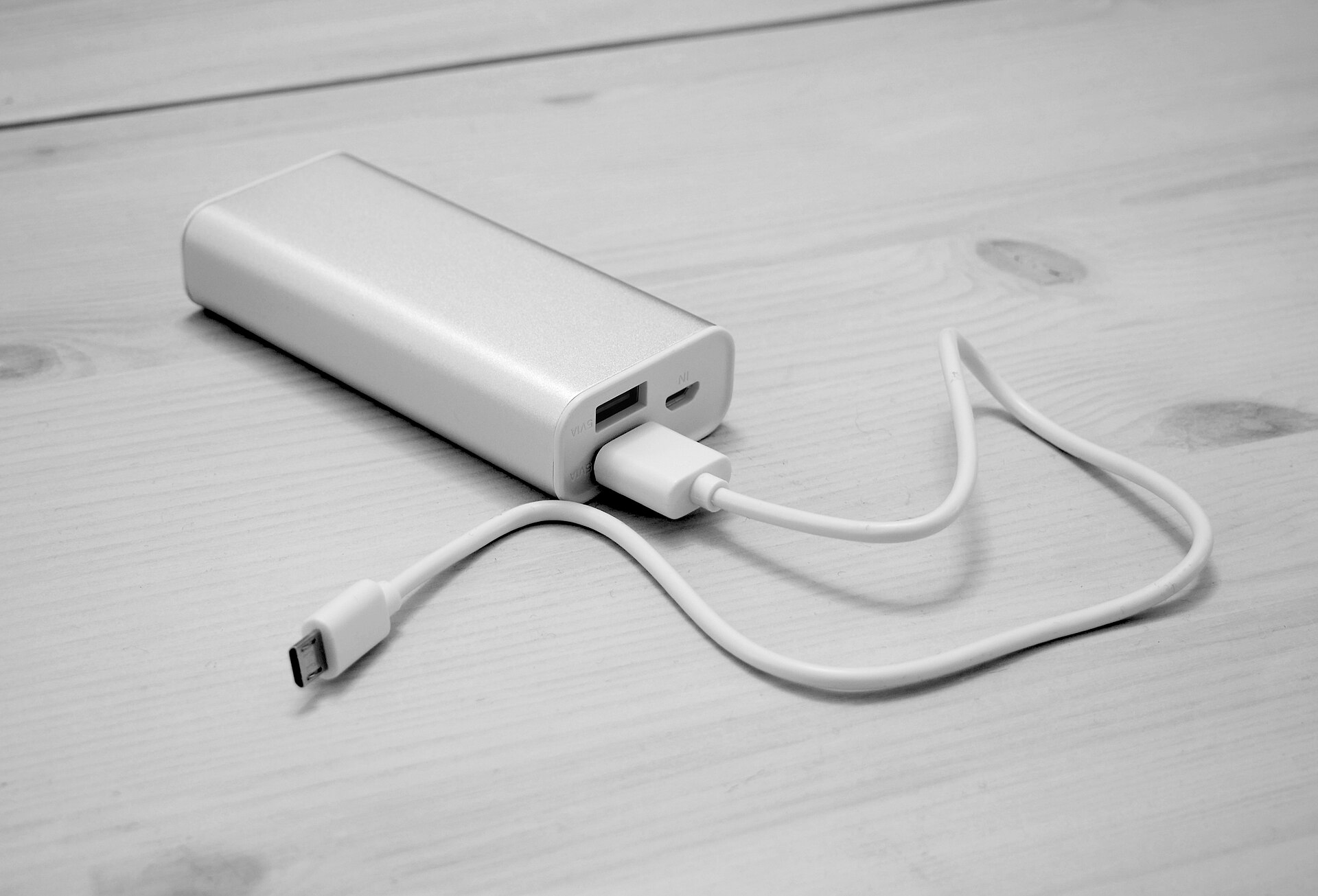 A slim power bank on a wooden table with a USB cable plugged in