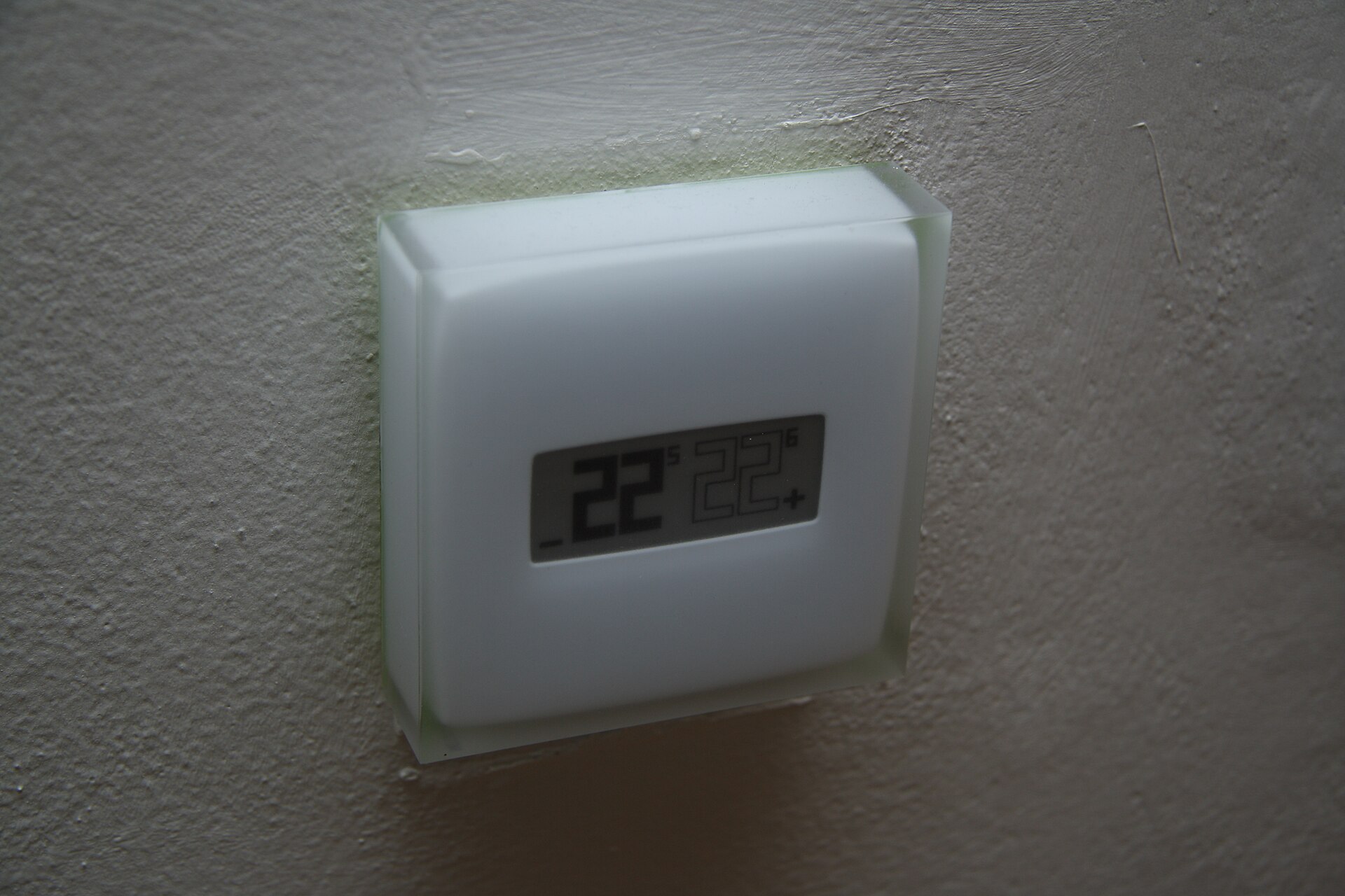 A white smart thermostat with a simple digital display mounted on a textured wall
