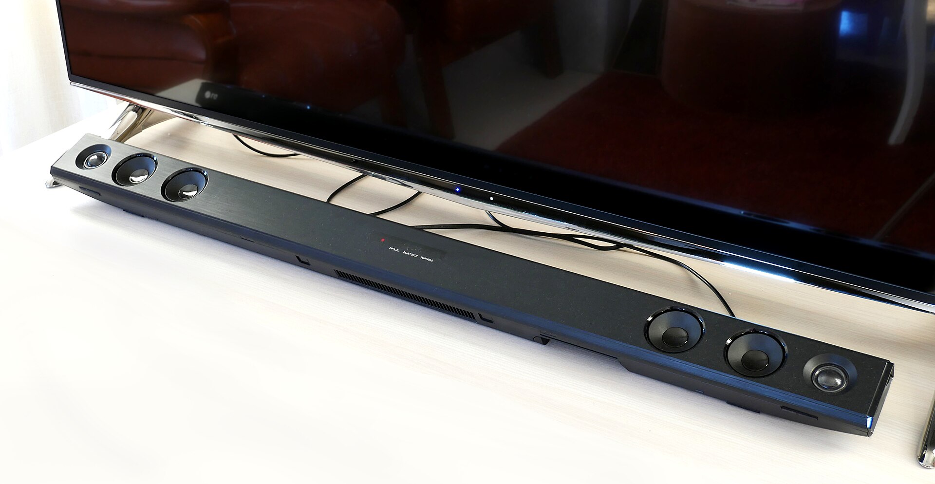 Slim soundbar with exposed drivers in front of a television