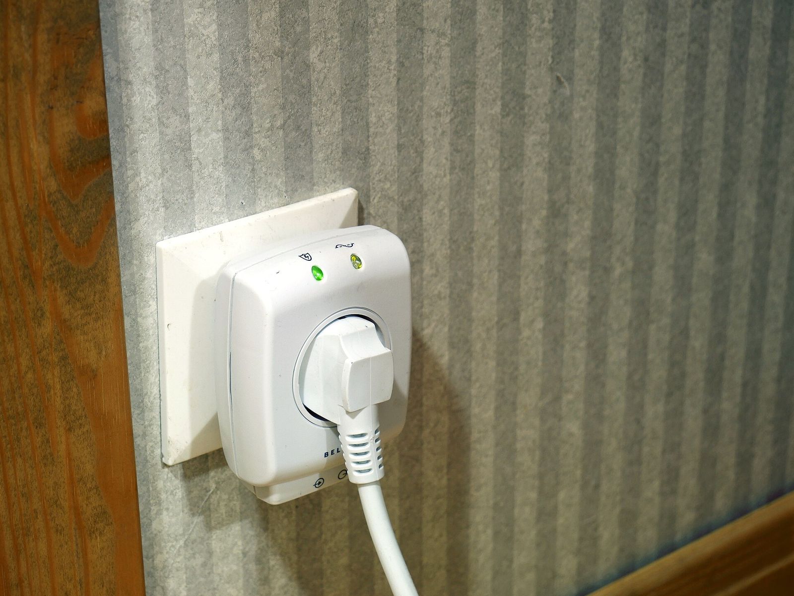 A white plug-in surge protector with two indicator lights fitted to a wall socket