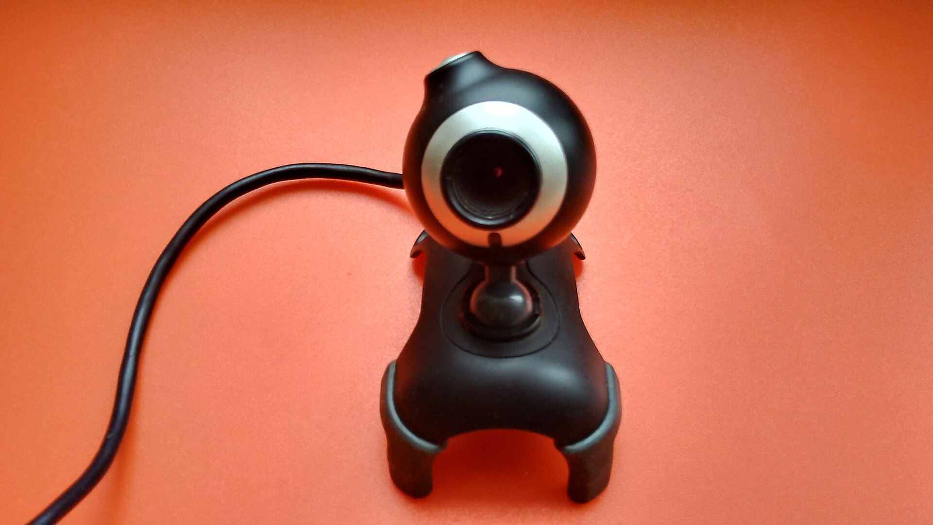 A small USB webcam on a stand against an orange background
