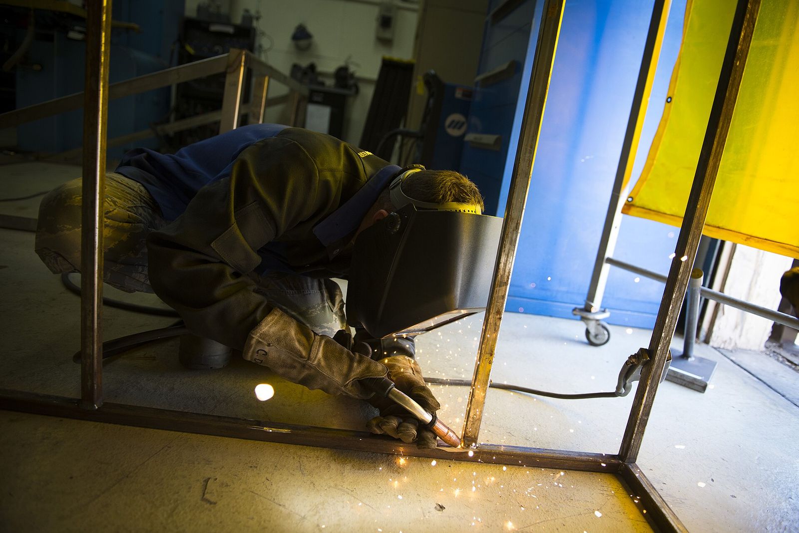 A welder in a helmet and leather gloves welding a steel frame