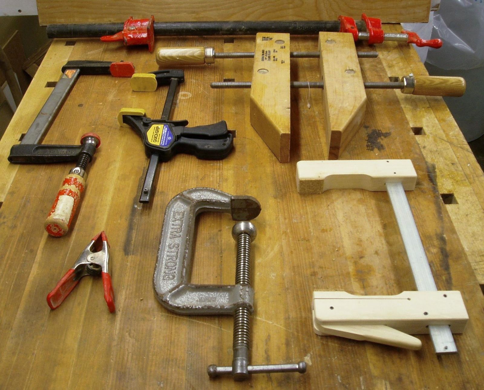 Pipe, F-style, one-handed bar, handscrew, spring and C-clamps laid out on a wooden workbench