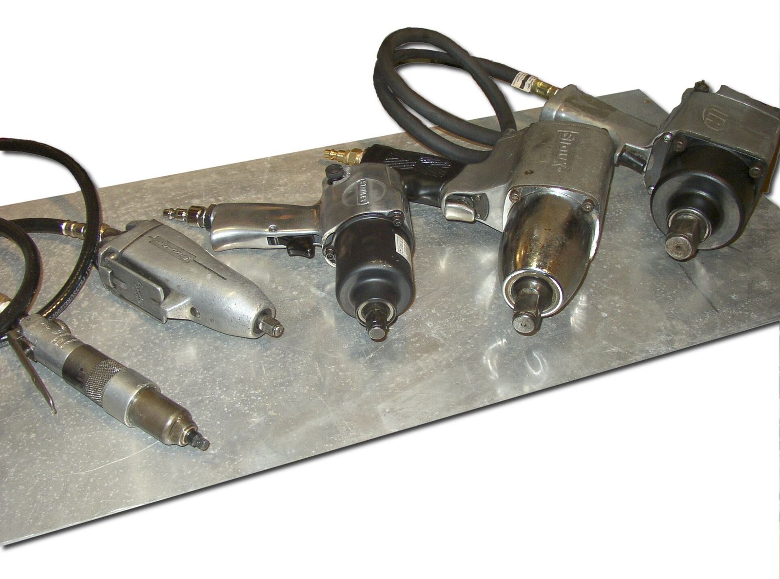 Several pneumatic impact wrenches of different sizes with air hoses on a metal sheet