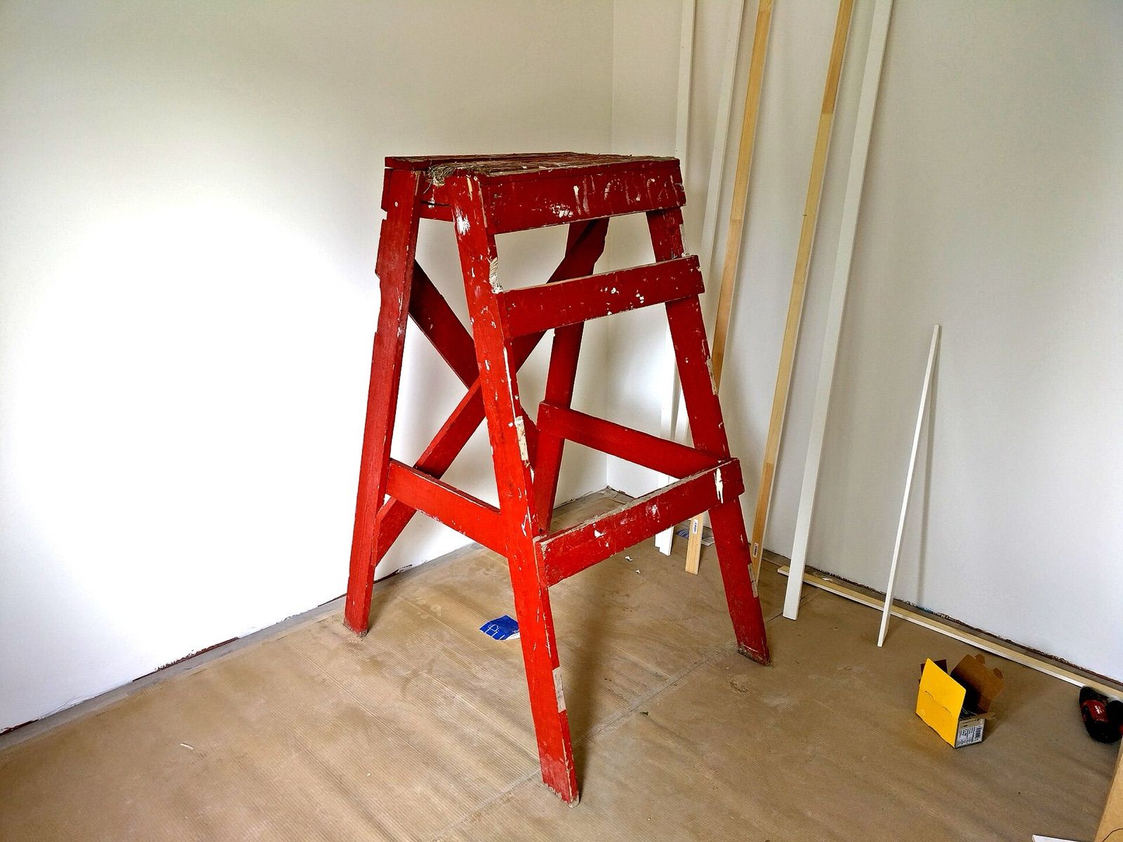 A paint-spattered red wooden stepladder standing in the corner of a room being decorated