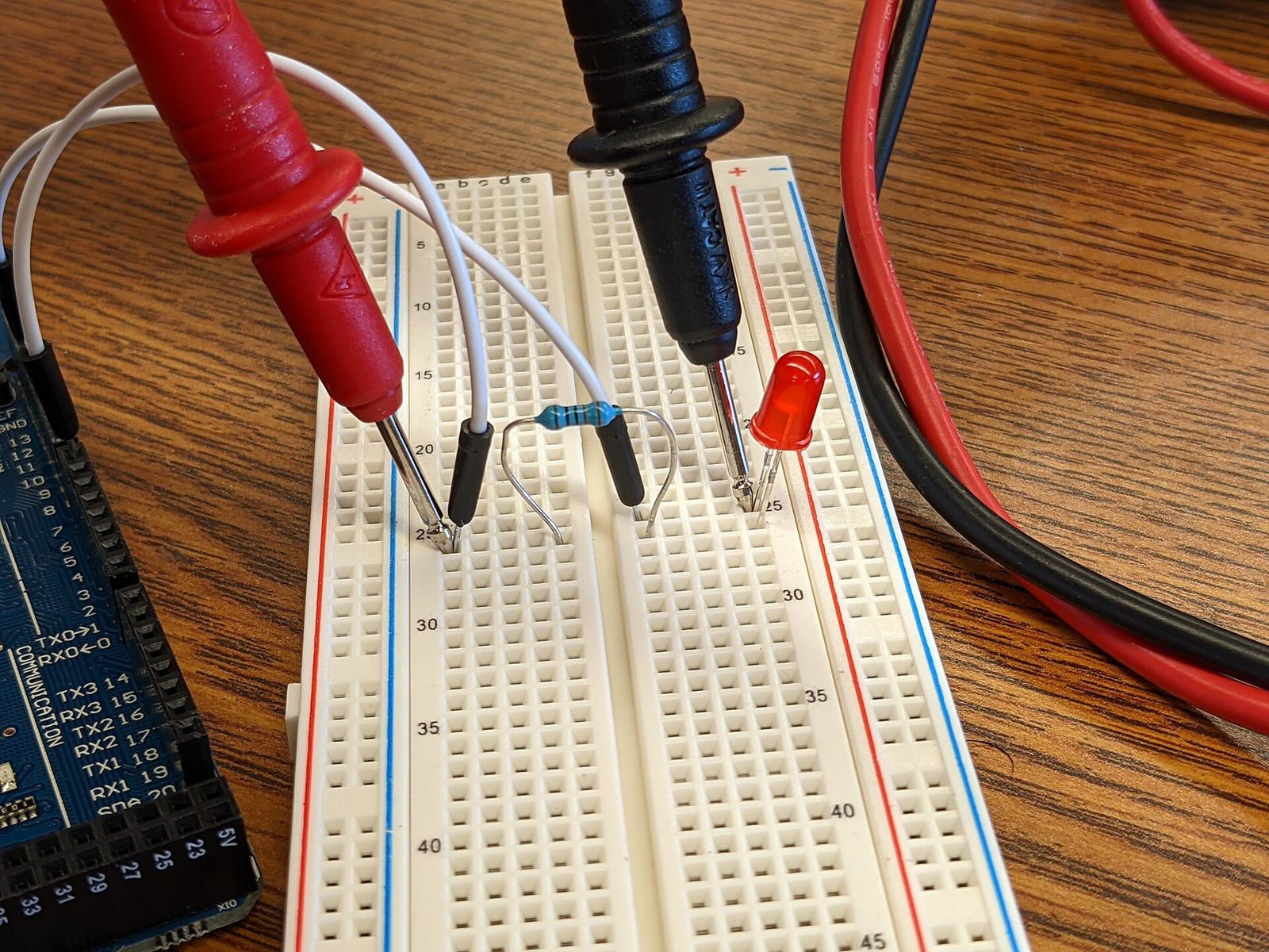 Red and black multimeter probes touching a resistor circuit on a breadboard